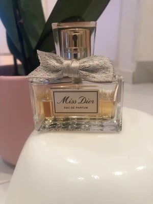 Miss Dior Eau de Parfum 50ml - Miss Dior Eau de Parfum från Dior i en elegant glasflaska med guldfärgad spray och en dekorativ silverfärgad rosett. Flaskan har en klassisk rektangulär form och etikett framtill. Doften är feminin och tidlös. Hälften av innehållet är kvar alltså 15mm av totalt 30mm😊