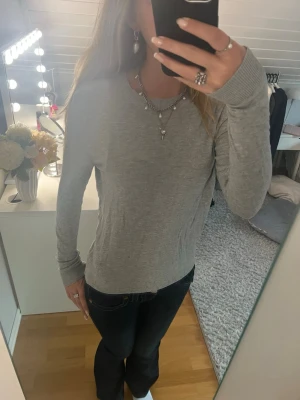 Ljusgrå långärmad tröja - En enkel och stilren ljusgrå långärmad tröja i mjukt material. Tröjan har rund halsringning och en rak passform som passar till det mesta. Perfekt basplagg för garderoben och lätt att matcha med olika stilar.