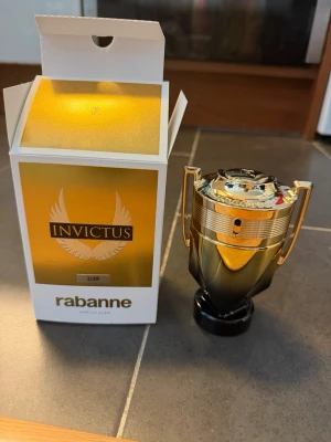 Invictus Elixir parfym från Rabanne - Säljer en Invictus Elixir parfym från Rabanne. Flaskan har en unik pokalform i guld och svart, vilket ger en lyxig känsla. Förpackningen är vit och guld med tydlig logga och vingar. Perfekt för dig som vill sticka ut med en exklusiv doft.