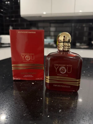Armani Stronger With You Tobacco  - Stronger With You Tobacco från Emporio Armani är en exklusiv parfym i en mörkröd glasflaska med gulddetaljer och rundad guldfärgad kork. Doften har en lyxig och elegant känsla, och flaskan rymmer 100 ml. Perfekt för dig som gillar unika och djupa doftnoter.