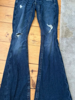 Blå bootcut jeans från Gina Tricot - Säljer ett par blå bootcut jeans från Gina Tricot i storlek XS. Jeansen har slitna detaljer och råa kanter för en trendig look. Klassisk femficksmodell med vita kontrastsömmar och låg midja. Perfekta för dig som gillar retrostil! Nypris 400 och pris går att diskutera 