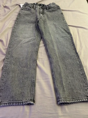 Grå raka jeans med hög midja - Säljer ett par grå tvättade jeans med rak passform och hög midja. Jeansen har klassiska fem fickor och bälteshällor. Materialet är kraftig denim som ger en cool vintagekänsla. Perfekta till sneakers eller boots.