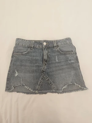 Jättesnygg blå jeanskjol från Gina Tricot, 152 - Säljer en blå jeanskjol från Gina Tricot i klassisk denim med råa kanter och slitna detaljer. Kjolen är i storlek 152 men passar xxs/xs också. Kjolen är använd några gånger, men är ändå i väldigt fint skick. OBS. Se sista bilden, det finns en liten slitning. 