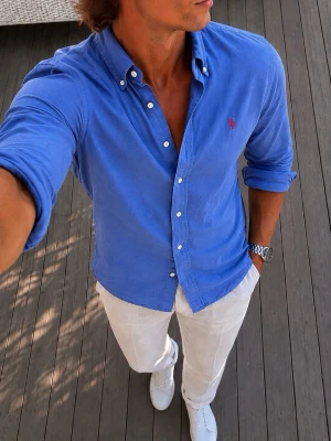 Ralph Lauren skjorta med knappar - Säljer en klassisk blå Ralph Lauren skjorta med button-down krage och vita knappar. Skjortan har lång ärm och en liten röd broderad logga på bröstet. Perfekt till jeans eller chinos för en clean och stilren look.