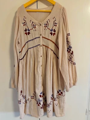 Beige broderad klänning från Zara  - Zara-klänning från 2024 års kollektion, beige med röda, blå och lila blombroderier. Den har en bohemisk stil och en volangkantad fåll.       Perfekt för sommaren 🍦🥂☀️🏖️🌅 