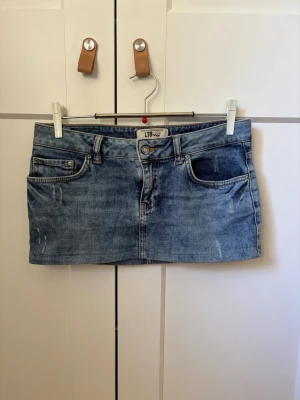 Blå jeansminikjol från LTB - Säljer en snygg blå jeansminikjol från LTB med klassisk femficksdesign, bälteshällor och slitna detaljer. Kjolen har en rak passform och är gjord i mjukt denimtyg.