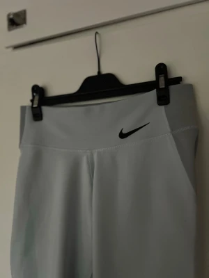 Ljusgrå leggings från Nike - Ljusblå träningstights från Nike med låg midja och svart logga på vänster sida. Tillverkade i ett stretchigt material som sitter tajt och är perfekta för gymmet! 