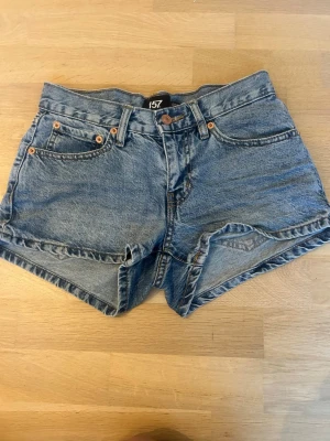 Blå jeansshorts - Säljer ett par klassiska blå jeansshorts med lågmidja och fem fickor. Shortsen har bälteshällor, knapp och dragkedja framtill. Perfekta till sommaren och lätta att matcha med olika stilar.