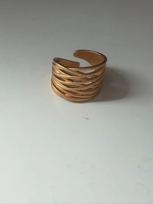 Bred flätad guldfärgad ring - Snygg bred ring i guldfärg med flätad design och öppen baksida som gör den justerbar. Ringen har en matt finish och passar perfekt för dig som gillar trendiga accessoarer med lite extra attityd. Materialet ser ut att vara metall.