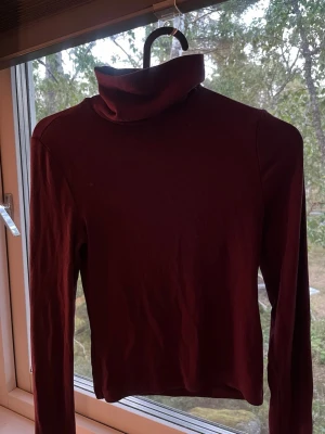 Vinröd polotröja från H&M!! - Säljer en vinröd polotröja med långa ärmar och ribbad struktur. Tröjan har en polokrage, perfekt att styla med jeans eller kjol. Materialet är mjukt och stretchigt. 