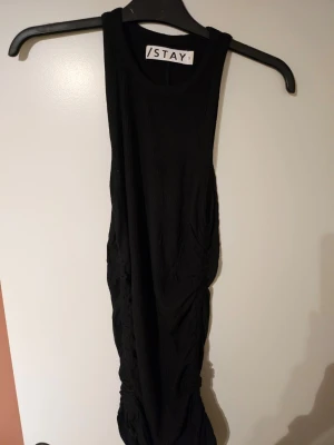 Svart klänning med snörning - Säljer en svart klänning från Stay med ärmlös design och snygg snörning längs sidan. Klänningen har en tight passform och är tillverkad i ett mjukt, ribbat material som ger en cool och modern look.