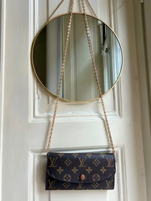 Klassisk monogram long wallet / crossbody - Ikoniskt monogrammönster och guldfärgad kedjerem. Väskan har en elegant, rektangulär form och stängs med en knapp framtill. Separat inköpt kedja + inlägg medföljer kostnadsfritt.