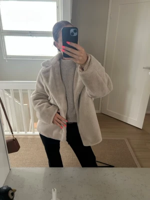 Beige fluffig pälsjacka - Säljer en beige, fluffig pälsjacka med bred krage och avslappnad passform. Jackan är gjord i mjukt fuskpälsmaterial och har en stilren look som passar perfekt till kalla dagar. Enkel att matcha med olika outfits och riktigt cozy.