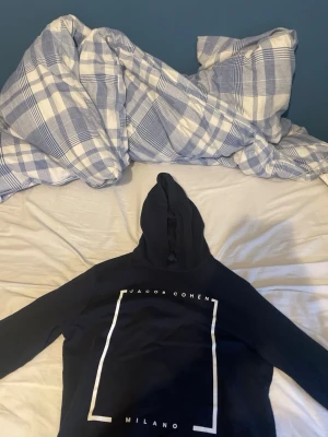 Marinblå hoodie från Jacob Cohën - Snygg marinblåhoodie från Jacob Cohën med vit text och grafiskt tryck på bröstet. Tröjan har huva och långa ärmar, perfekt för en avslappnad och trendig stil. Milano-detalj framtill ger en exklusiv känsla.