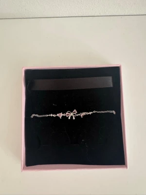 Pandora armband  - Sött armband från Pandora med tunna silverfärgade kedjor och dekorationer av små rosa  diamanter samt en rosett i mitten. Perfekt accessoar för dig som gillar en feminin och elegant stil. Levereras i original ask. Helt ny och säljs för att jag har bytt till guld, pris kan diskuteras!🥰
