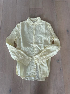 Linneskjorta från Uniqlo - Säljer en ljusgul skjorta från Uniqlo i 100% linne. Skjortan har klassisk krage, knäppning framtill och långa ärmar. Perfekt för dig som gillar en avslappnad men ändå stilren look.
