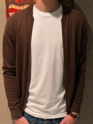 John Henric helzip - Säljer en stilren brun helzip i merinoull från John Henric. Perfekt att slänga över en t-shirt eller skjorta. Modellen är ungefär 185cm