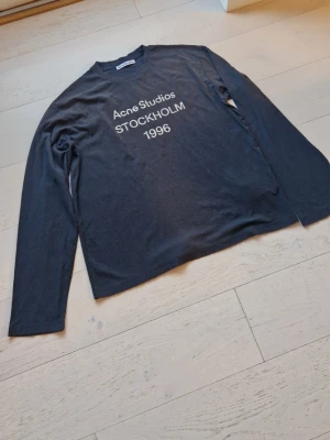 Svart långärmad topp Acne Studios - Cool svart långärmad topp från Acne Studios med tryck 'Acne Studios STOCKHOLM 1996' på bröstet. Tillverkad i mjuk bomull och har en klassisk rund hals. Perfekt för en avslappnad och trendig look.