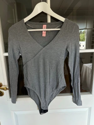 Grå ribbad omlott-body  - Jättefin och skön långärmad body i gråmelerat, ribbat tyg från Hunkemöller. Den har en v-ringning och knäppning i genen med tryckknappar. Perfekt som basplagg💫