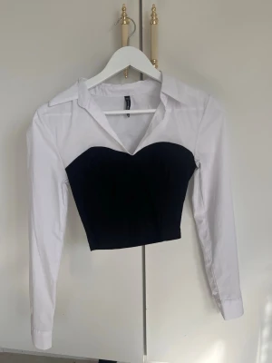 Vit och svart långärmad blus - Snygg långärmad blus med vit skjortkrage och ärmar samt svart. Blusen har en hjärtformad byst och klassisk skjortdetalj upptill. Köpt på new yorker, storlek: S
