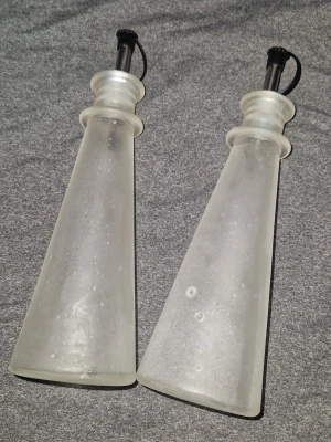olje- och vinägerflaskor - Snyggt och dekorativt set med två flaskor/karaffer i frostat glas, perfekt för olja, vinäger eller dressing. Flaskorna har en elegant, konisk form utrustad med en praktisk hällpip och lock. Mycket fint skick!