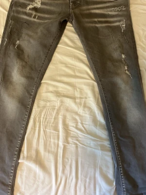 Grå jeans DSQ2 - Säljer ett par grå jeans från DSQ2 med slitningar och distressed detaljer på både fram- och baksidan. Jeansen har raka ben och klassiska fickor bak. Perfekt för dig som gillar en edgy och trendig look.