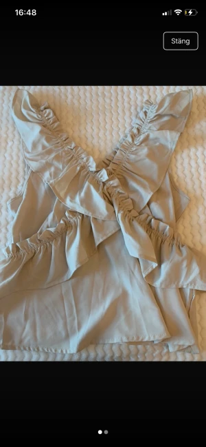 Beige omlottopp med volanger - Supersöt beige omlottopp med volangdetaljer och djup v-ringning. Toppen är ärmlös och har en luftig passform, perfekt för varma dagar. Styla med jeans eller kjol för en trendig look.