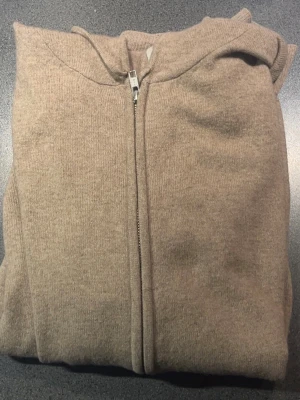 Kashmir hoodie med dragkedja John Henric - Mjuk och stilren beige hoodie från John Henric med dragkedja framtill och två fickor. Tillverkad i 100% kashmir material och har en klassisk huva. Perfekt för en avslappnad look och enkel att matcha med andra plagg.
