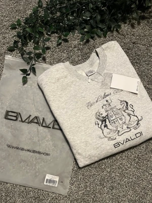 Grå sweatshirt från BVALDI - Ny grå sweatshirt från BVALDI med tryck framtill som visar ett stilrent vapensköld-motiv och texten 'Côte d'Azur Club'. Tröjan har rund halsringning, ribbade muddar och är tillverkad i mjukt material för maximal komfort. Perfekt för en avslappnad och trendig look. Storlek S, passar de som är ca 170cm! 