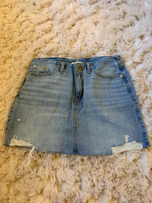 Blå jeanskjol med slitna detaljer - Trendig blå jeanskjol i kort modell med slitna detaljer och rå kant nertill. Klassisk femficksdesign och bälteshällor. Perfekt för en avslappnad och cool stil. Storlek 164 men är för stor för mig som vanligtvis har 32/xxs/xs.