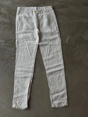 NN07 Premium Linen Trousers – Sand / Off-White (W30/L34) - Snygga beiga linnebyxor med smal passform och hög midja. Byxorna har fickor fram och bak, stängs med knapp och dragkedja. Perfekta för en avslappnad och stilren look. Tillverkade i luftigt linne som känns svalt och skönt.