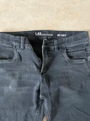 Mörkgrå slim fit jeans LAB Industries - Snygga mörkgrå slim fit jeans från LAB Industries. Modellen heter LUKE och har klassisk femficksdesign, bälteshällor och dragkedjegylf. Jeansen har en smal passform och är tillverkade i ett stretchigt material för extra komfort. Jag hade sagt de passar lite som skinny jeans
