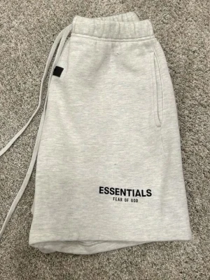 Grå Essentials shorts FÖRBESTÄLLING ENDAST  - Snygga ljusgrå shorts från Fear of God Essentials med elastisk midja och snörning. Shortsen har fickor på sidorna och logga tryckt framtill. Perfekta för en avslappnad och trendig stil. Helt nytt fraktar inom 24 timmar 