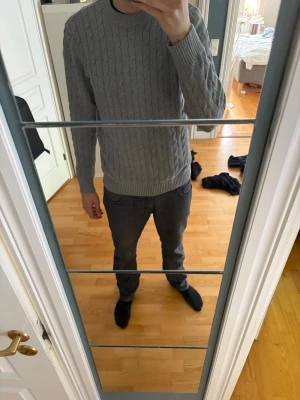 Grå kabelstickad tröja Selected Homme - Snygg grå kabelstickad tröja från Selected Homme med rund halsringning och ribbade muddar. Tröjan har ett klassiskt flätmönster och är perfekt för lager på lager. Tillverkad i mjukt material som känns skönt mot huden. Hör av dig vid funderingar