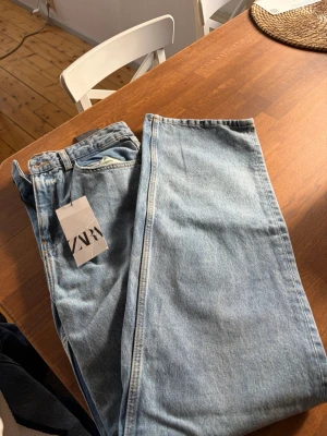 Ljusblå raka jeans från Zara - Säljer ett par ljusblå jeans från Zara med rak passform och klassisk femficksdesign. Jeansen har hög midja och är tillverkade i ett mjukt denimtyg. Perfekta för en avslappnad och trendig look.