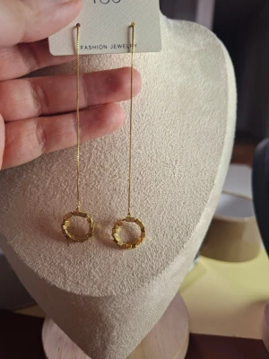 Guldiga långa örhängen med cirklar - Säljer ett par trendiga guldiga örhängen med tunn kedja och geometriska cirklar längst ner. Örhängena har en minimalistisk och modern design som passar perfekt till en stilren look. Materialet är metall med guldfinish.