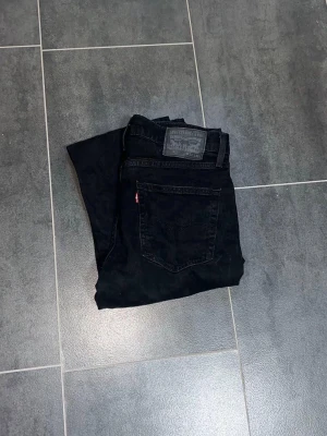 Svarta Levi's 527 bootcut  jeans - Säljer ett par klassiska svarta Levi's 527 jeans med straight fit och femficksmodell. Jeansen har knappgylf och den ikoniska röda Levi's-lappen på bakfickan. Tillverkade i slitstark denim, perfekta för en clean och tidlös look.