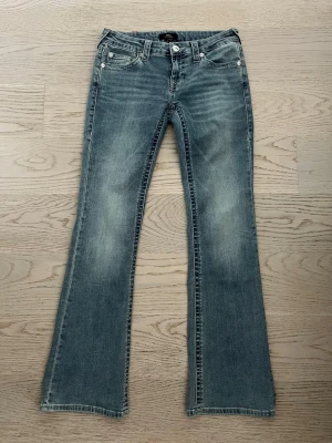True Religion ljusblå bootcut jeans  - Ljusblå bootcut jeans från True Religion med klassisk broderad logga på bakfickorna och snygga slitningar framtill. Jeansen har fem fickor, låg midja och är tillverkade i denim med stretch för skön passform.