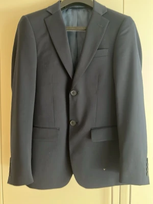 Dressman kavaj - Stilren svart kavaj från Dressmann i modellen Slim Fit. Klassisk design med två knappar framtill, smala slag och tre fickor. Perfekt för dig som vill ha en modern och snygg look. Fodrad insida med diskreta detaljer.