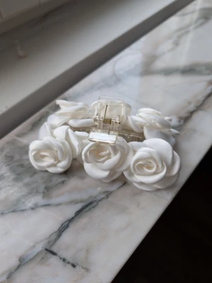 Vit hårklämma med tygrosor - Säljer en superfin hårklämma dekorerad med vita tygrosor. Klämman är genomskinlig och har flera mjuka blommor i tyg som ger en romantisk och trendig look. Perfekt accessoar för att piffa upp frisyren och skapa en söt vibe.