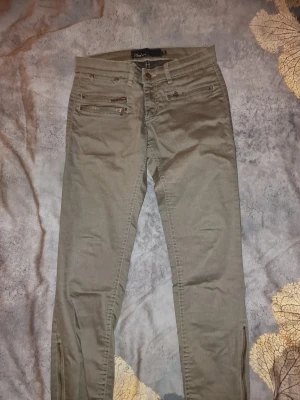 Olivgröna byxor med dragkedjor - Byxorna har dekorativa dragkedjor framtill och även vid besluten. Snyggt till sommaren. 