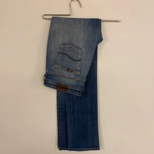 Blåa jeans från Lee - Snygga blå bootcut jeans från Lee med klassisk femficksdesign och ljusa slitningar framtill. Jeansen har en läderpatch med logga bak och är tillverkade i ett mjukt denimtyg. Perfekta för en avslappnad och trendig look.