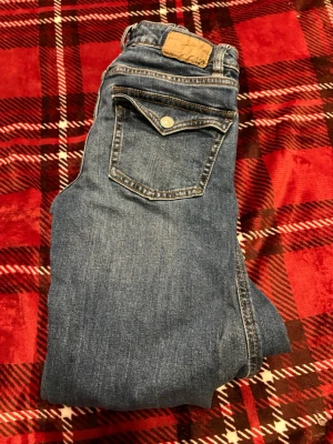 Blå jeans från 157, storlek XS - Säljer ett par klassiska blå jeans från 157 i storlek XS med full längd. Jeansen har en snygg bakficka med knappdetalj och kontrastsömmar. Perfekta till vardagslooken och passar till det mesta. Materialet är slitstarkt denim.