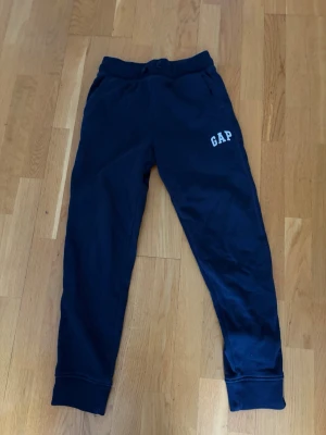 Mörkblå mjukisbyxor från GAP - Snygga mörkblå mjukisbyxor från GAP med resår i midjan och muddar vid bensluten. Byxorna har två sidofickor och GAP-logga tryckt på vänster lår. Perfekta för chill dagar eller när du vill vara bekväm. Tillverkade i mjukt bomullsmaterial.
