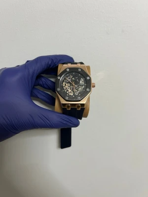 Svart och guld klocka från Casiru - Stilren klocka från Casiru med svart urtavla och synlig mekanik. Boetten är i guldtonad metall med sex skruvar på ramen och svart kant. Svart armband i syntetmaterial. Perfekt accessoar för dig som gillar detaljer och modern design. Helt ny aldrig använt den snabb leverans följ oss för 12% rabatt 