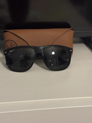 Svarta Ray-Ban solglasögon - Klassiska svarta Ray-Ban solglasögon med mörka glas och ikonisk logga på linsen. Medföljer ett brunt Ray-Ban fodral i skinnimitation.  Köpta på synsam för 2300 använda cirka 6 gånger