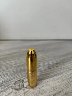 MAC läppstift i guldig hylsa - Snyggt läppstift från MAC i en exklusiv guldig hylsa. Färgen är en djup röd nyans med matt finish. Hylsan har en rundad form och känns lyxig och trendig. Perfekt för dig som vill ha ett statement-läppstift i sminkväskan.