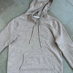 Grå hoodie från Brown Avenue - Mysig grå hoodie från Brown Avenue i storlek S. Tröjan har huva med snörning och en klassisk magficka framtill. Materialet är en ull och cashmere blandning köpt för 1800
