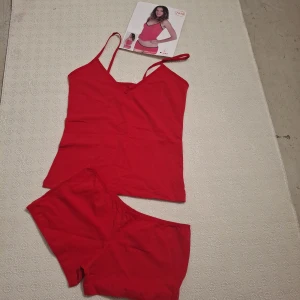 Röd linnetopp med smala axelband - Röd enkel linnetopp med smala axelband och v-ringning. Toppens material är mjuk bomull och den har en figurnära passform. Perfekt för att bära under andra plagg eller som den är under varma dagar.