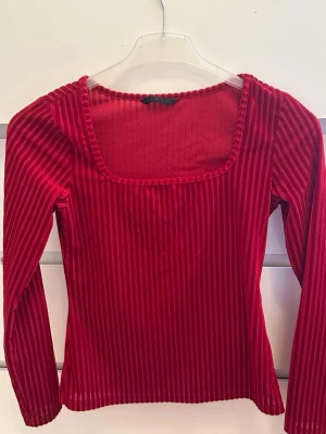 Röd ribbad långärmad topp - Snygg röd långärmad topp med ribbad struktur och fyrkantig ringning. Toppen har en figurnära passform och är perfekt för att lyfta vilken outfit som helst. Tillverkad i ett mjukt, stretchigt material som känns bekvämt hela dagen.